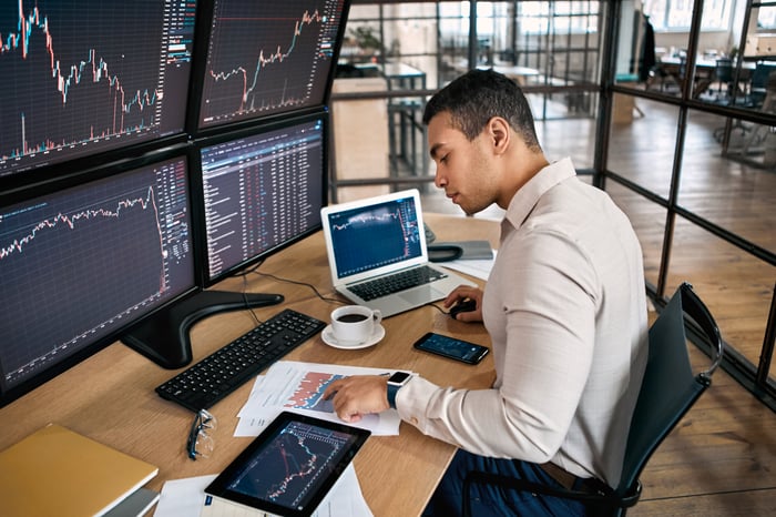 An investor sitting at a desk looking at several screens. 